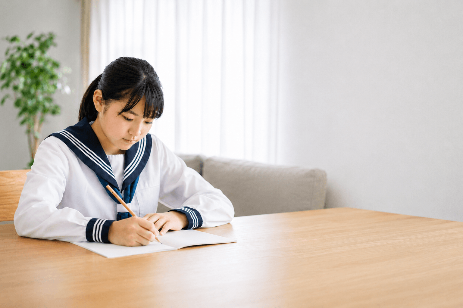 セーラー服の制服を着て机でノートに記入する生徒
